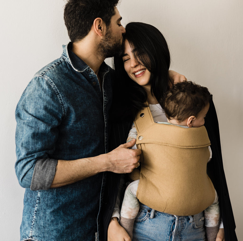 אישה עם תינוק במנשא ילקוט בצבע חרדל של חברת אורבן בייבי עם בן זוגה
