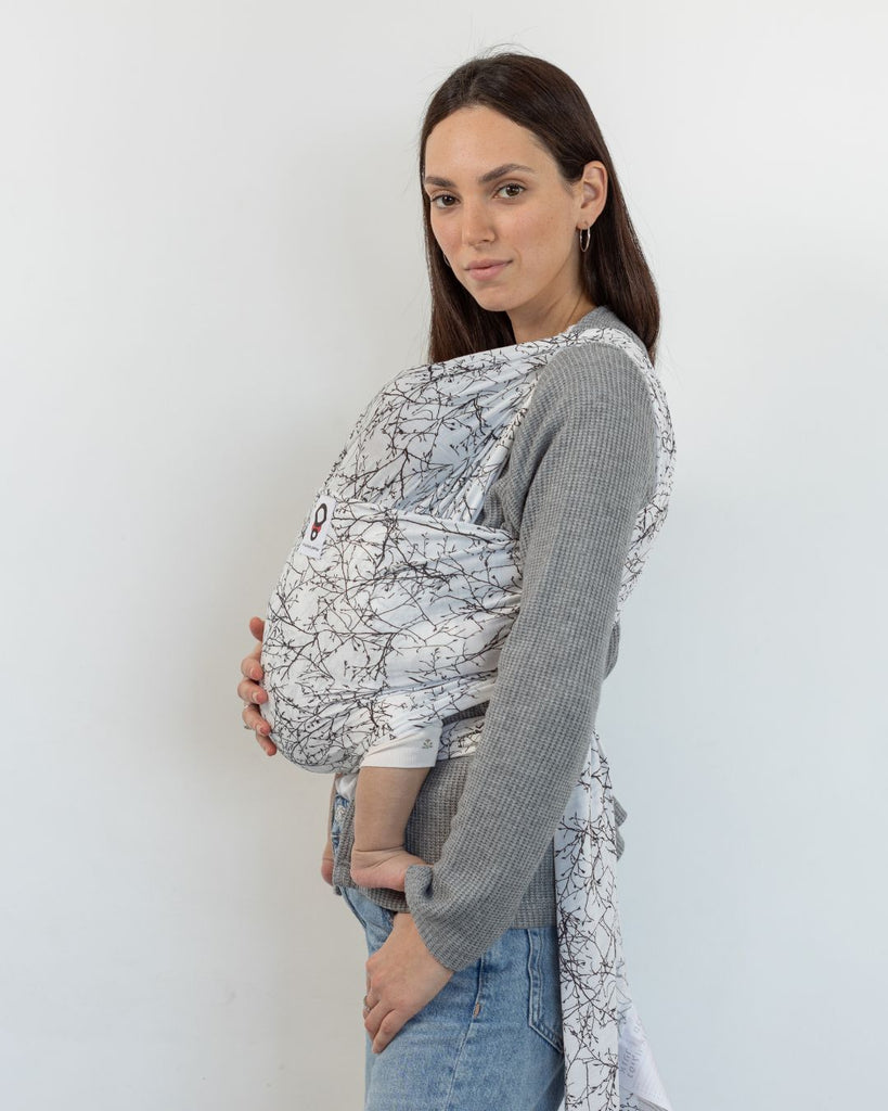 אישה עם תינוק במנשא קשירה מבד מגיל לידה מבד  מודל מדגם פורסט בצבע לבן עם הדפס של עלים ופרחים של חברת אורבן בייבי 