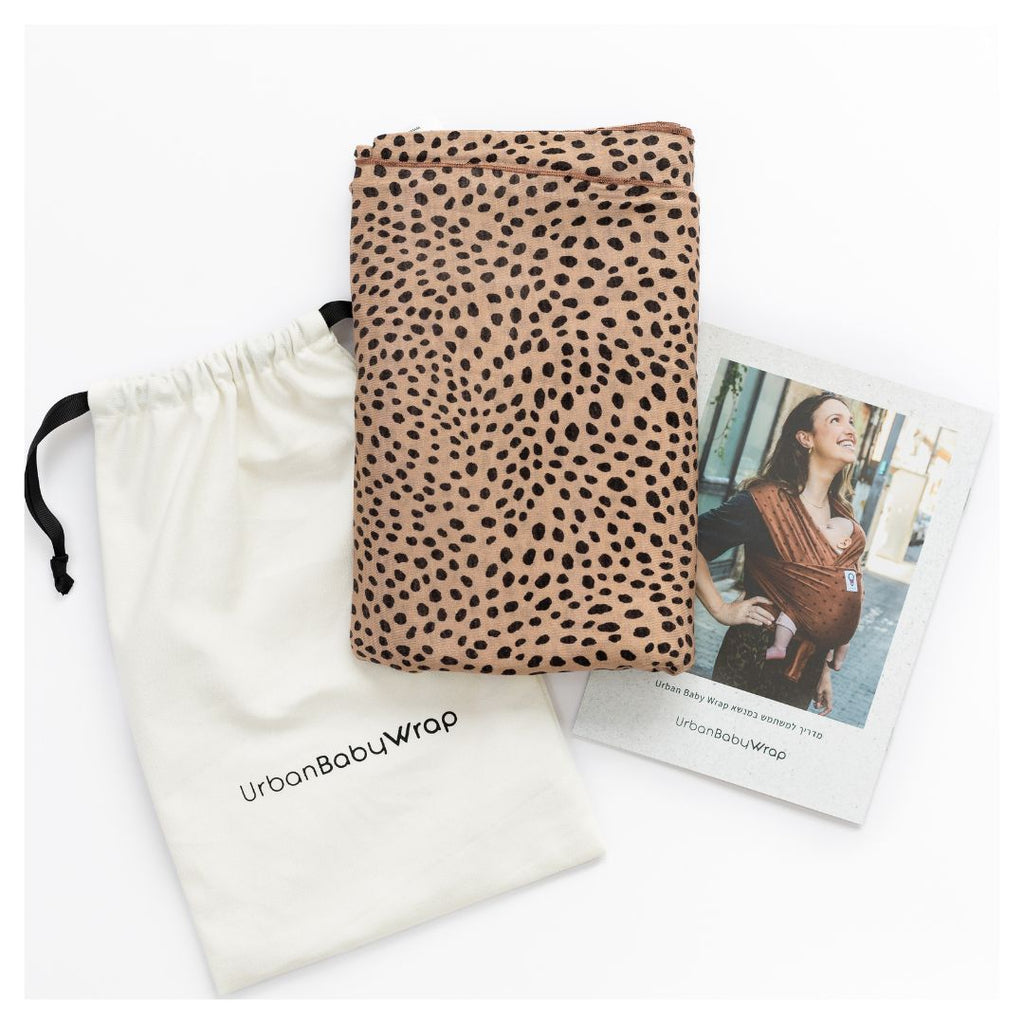 תמונת פק שוט של מנשא בד מגיל לידה של חברת אורבן בייבי מבד מודל בדוגמא צ'יטה בצבעים של רקע חול והדפס חברבורות שחורות ארוז כמתנת לידה עם שקית אחסון המדריך למשתמש 