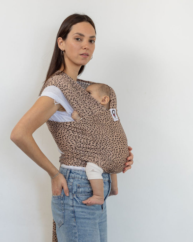 אישה עם תינוק במנשא קשירה מבד מגיל לידה מבד  מודל מדגם ציטה בצבע חול עם הדפס של מנומר וחברבורות של חברת אורבן בייבי 