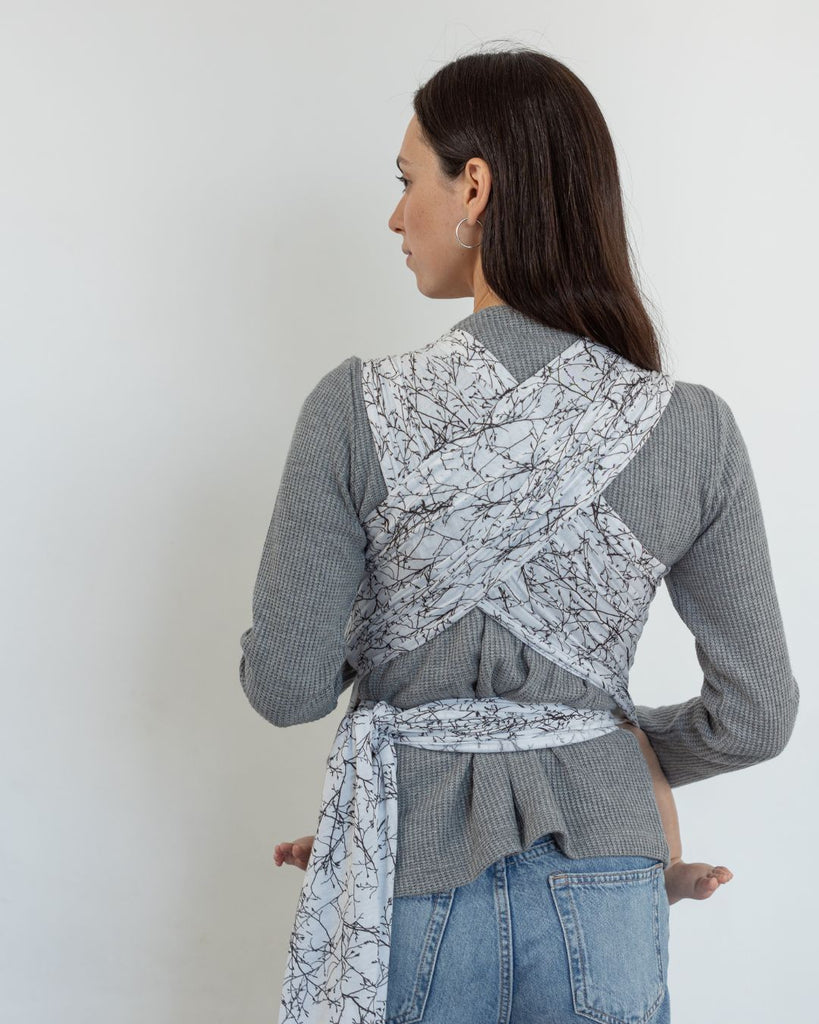 אישה עם תינוק במנשא קשירה מבד מגיל לידה מבד  מודל מדגם פורסט בצבע לבן עם הדפס של עלים ופרחים של חברת אורבן בייבי 