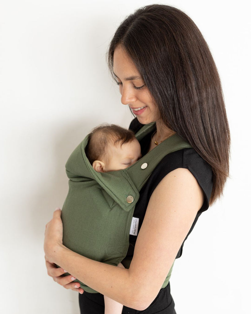 דוגמנית לבושה בבגדים שחורים נושאת תינוק במנח בטן לבטן עם מנשא תינוק בצבע ירוק מבד פשתן של חברת אורבן בייבי ראפ