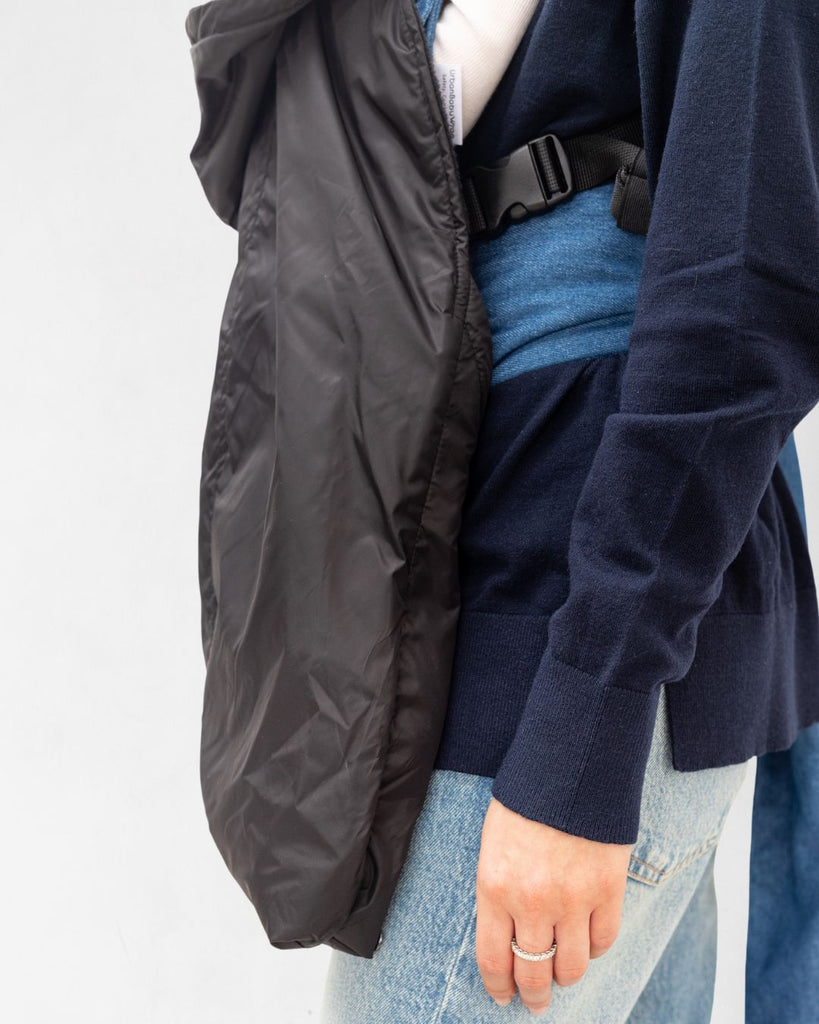 דוגמנית עם תינוק במנשא מכוסה במעיל מנשא לתינוק בצבע שחור עשוי שכבה חיצונית של ניילון ושכבה פנימית מפליז, כיסוי מנשא לתינוק לחורף במקום שמיכת מנשא