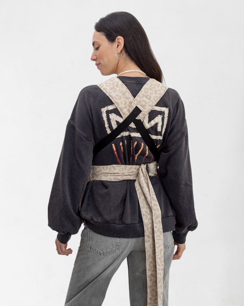 דוגמנית בתמונת גב נושאת תינוקת בת 11 חודשים במנשא ילקוט מגיל לידה בצבע אופוויט מבד פשתן טבעי עם הדפס מנומר של חברת אורבן בייבי ראפ במנח בטן לבטן  בעיצוב דומה לחברת ארטיפופ