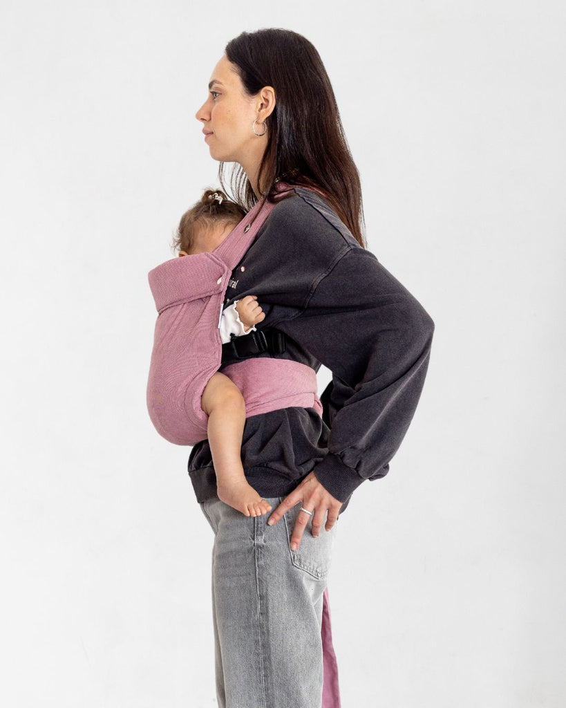 דוגמנית בתמונת פרופיל  נושאת תינוקת בת 11 חודשים במנשא ילקוט מגיל לידה בצבע ורוד עתיק מבד קורדרוי דק טבעי של חברת אורבן בייבי ראפ במנח בטן לבטן  בעיצוב דומה לחברת ארטיפופ