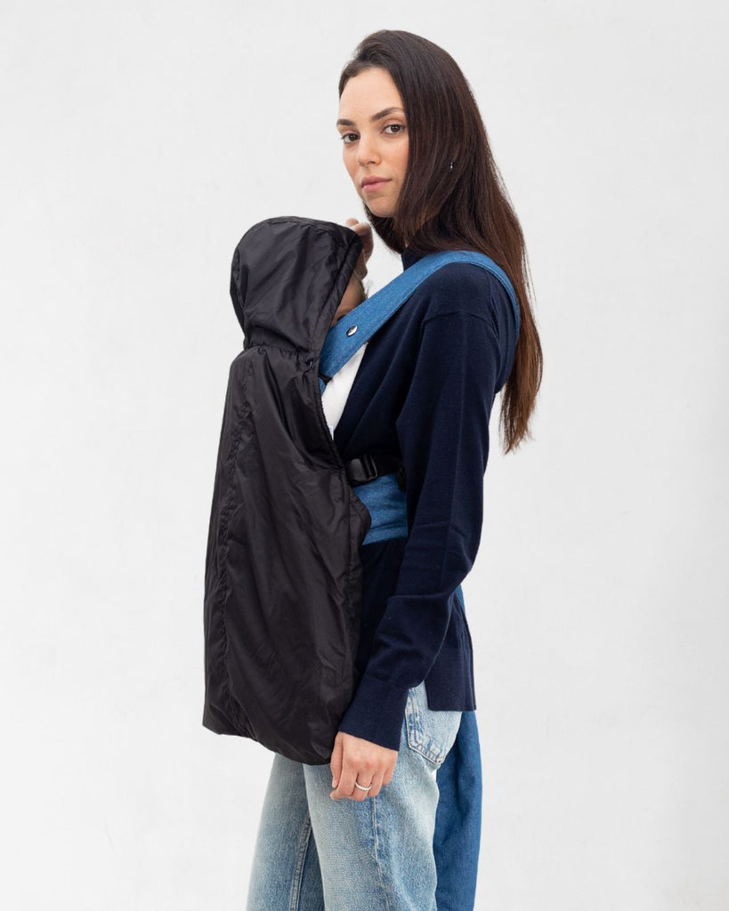 דוגמנית עם תינוק במנשא מכוסה במעיל מנשא לתינוק בצבע שחור עשוי שכבה חיצונית של ניילון ושכבה פנימית מפליז, כיסוי מנשא לתינוק לחורף במקום שמיכת מנשא