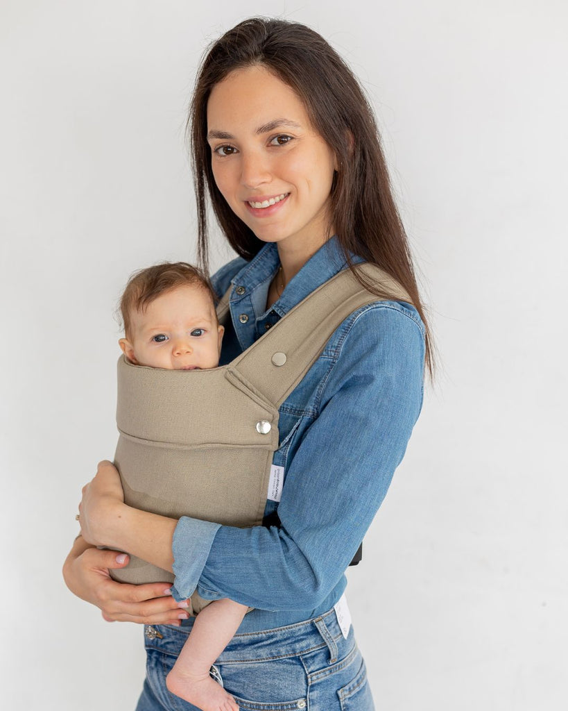דוגמנית בתמונה פרונטלית נושאת תינוקת בת 5 חודשים במנשא ילקוט מגיל לידה בצבע בז' מבד פשתן טבעי של חברת אורבן בייבי ראפ במנח בטן לבטן  