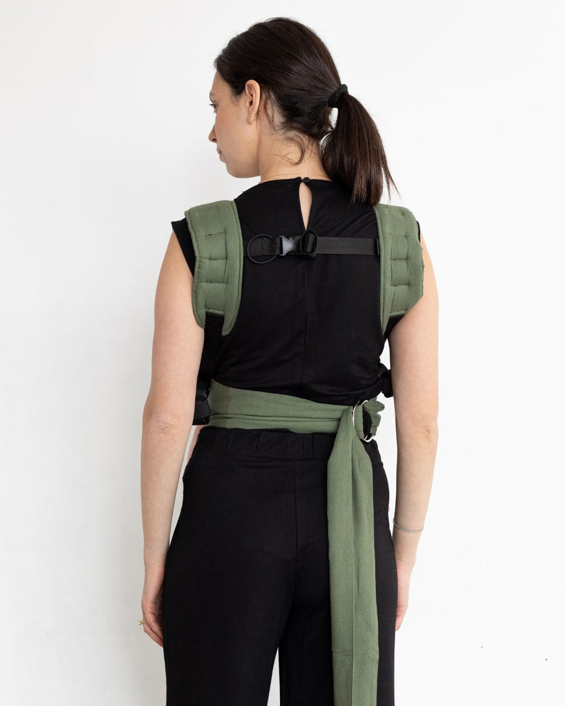 דוגמנית לבושה בבגדים שחורים נושאת תינוק במנח בטן לבטן עם מנשא תינוק בצבע ירוק מבד פשתן של חברת אורבן בייבי ראפ