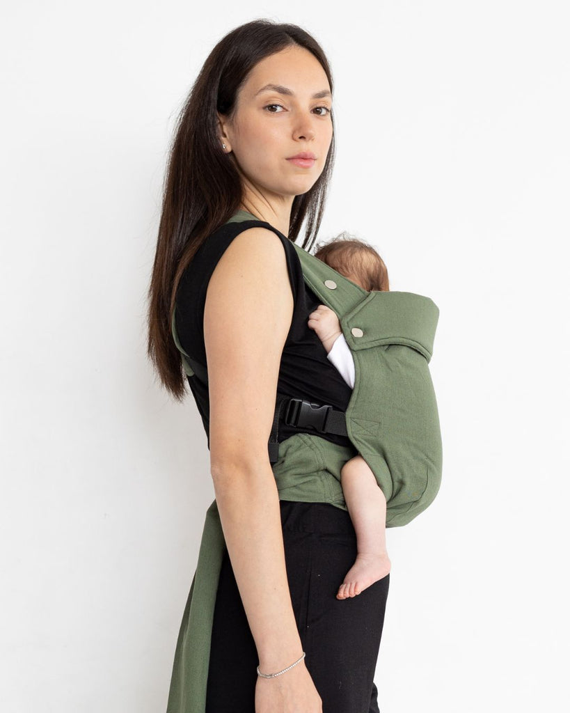 דוגמנית לבושה בבגדים שחורים נושאת תינוק במנח בטן לבטן עם מנשא תינוק בצבע ירוק מבד פשתן של חברת אורבן בייבי ראפ